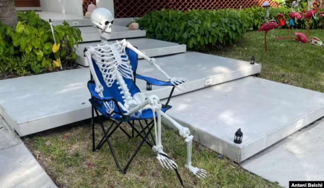 Una figura de un esqueleto sentado en una silla frente a una casa como parte de la decoración de Halloween en un barrio de Miami, Florida. (Foto: Antoni Belchi / VOA)