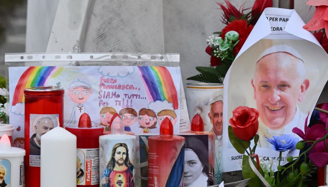 Velas, flores y un retrato del Papa Francisco se colocan en la estatua de Juan Pablo II afuera del hospital Gemelli, donde está hospitalizado el Papa Francisco, en Roma, el 24 de febrero de 2025.